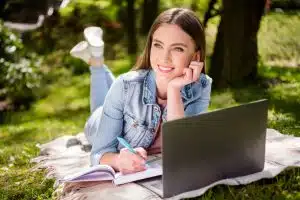 Female student using a laptop while laying down on the grass.