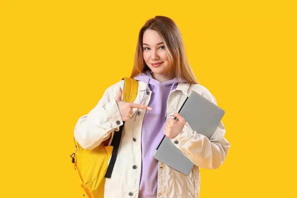 Female student smiling at the camera while holding her things.