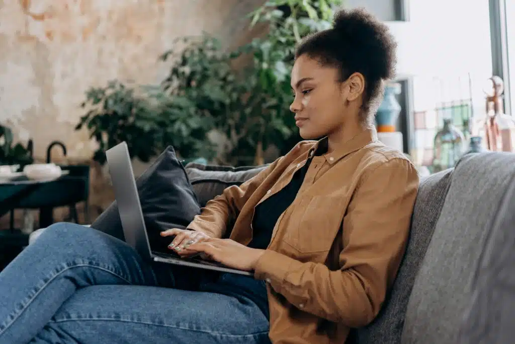 A young woman types on a laptop while sitting on a couch, possibly researching Johns Hopkins vs Columbia.