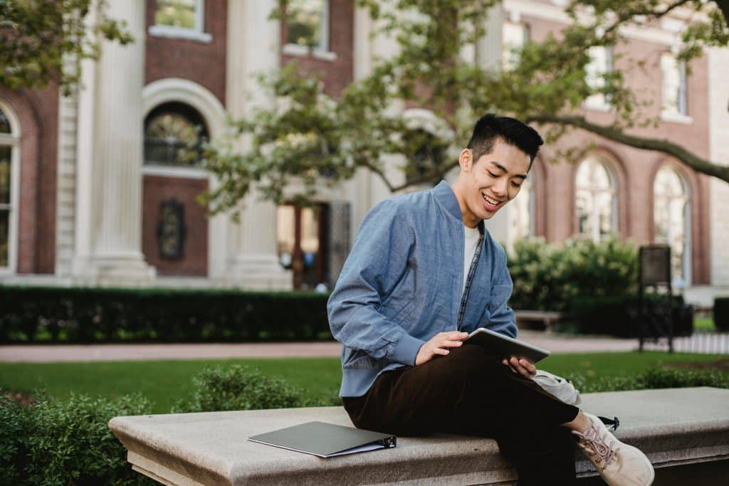 College student using a tablet on a campus lawn, representing a Brown vs USC comparison in campus life and academics