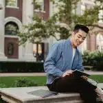 College student using a tablet on a campus lawn, representing a Brown vs USC comparison in campus life and academics