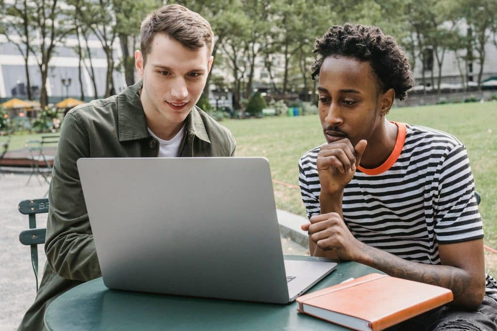 Two college students studying together on a laptop at an outdoor campus table, illustrating academic life in a Dartmouth vs Yale comparison.