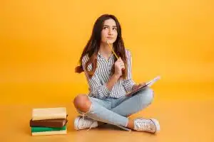 A student sitting with a lot of books on her side, thinking intently.