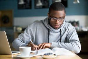 A male student studying and writing with a cup of coffee