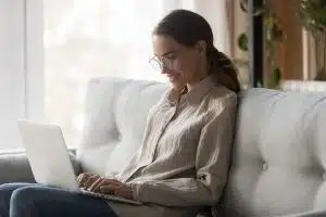 female student with glasses sitting on a couch while working with her laptop