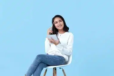 A student sitting on the chair, thinking intently while holding a notebook and pen.