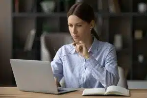 Confident, thoughtful woman looking at a laptop, holding her glasses