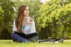 Thinking student sitting and holding a book in the park.