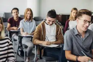 Group of high school students sitting in classroom and writing in notebooks.