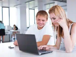 Two students talking in front of a laptop.