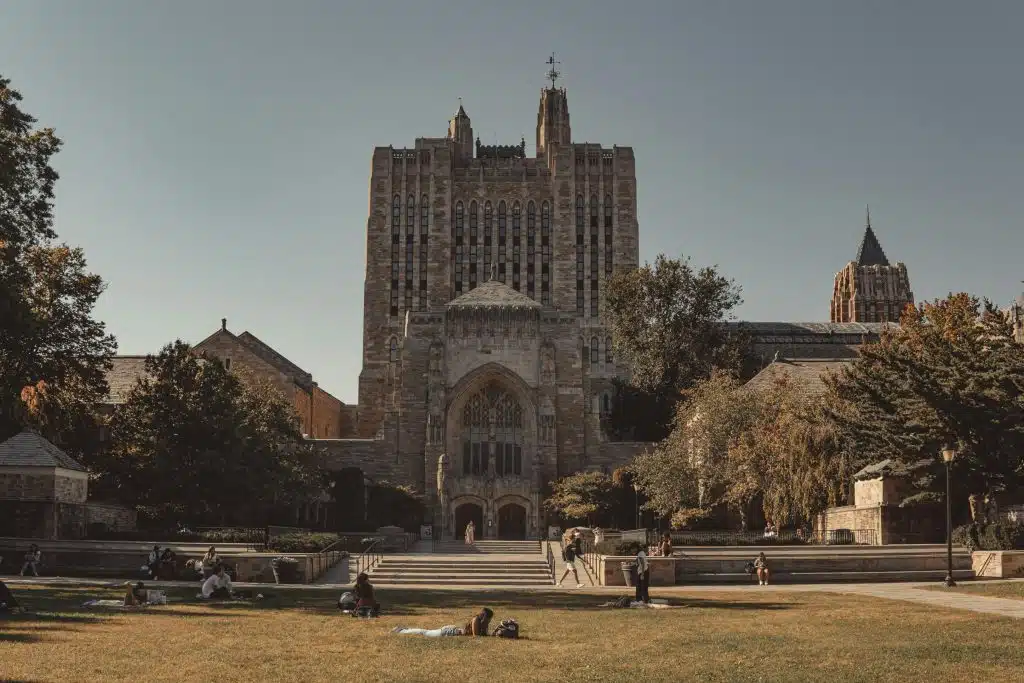 Yale campus with students relaxing on the lawn, highlighting the history and Yale traditions.