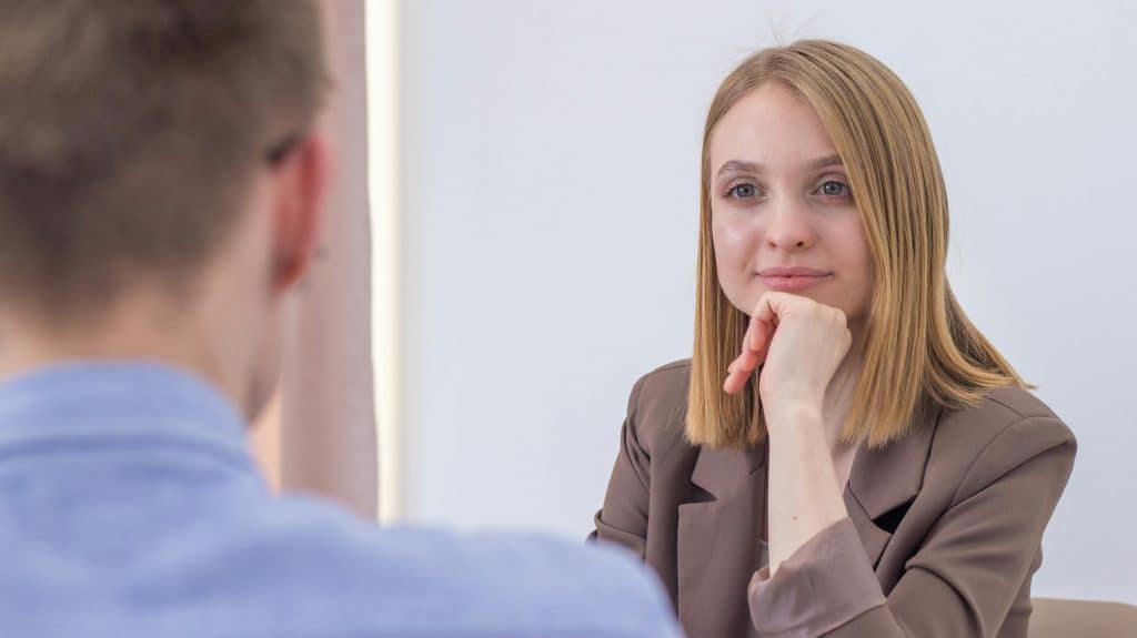A woman attentively listening during a grad school interview, resting her chin on her hand.