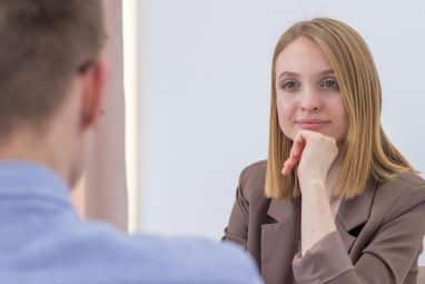 A woman attentively listening during a grad school interview, resting her chin on her hand.