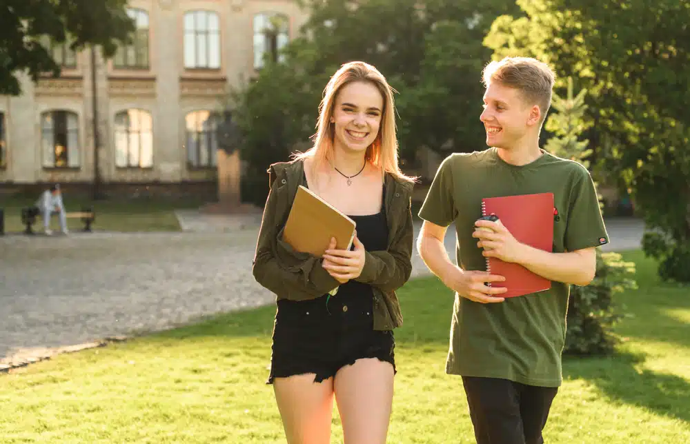 students walk at the college yard holding notebooks and smiling