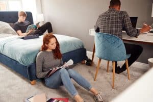 College students in shared house bedroom studying together