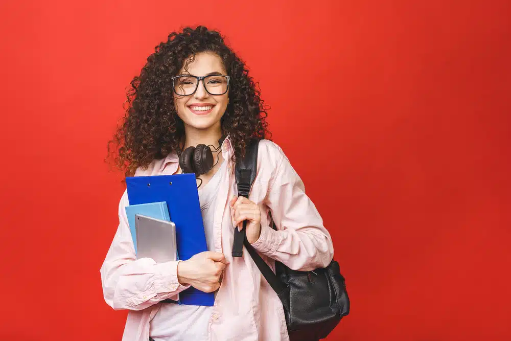 Young curly student woman wearing backpack glasses holding books