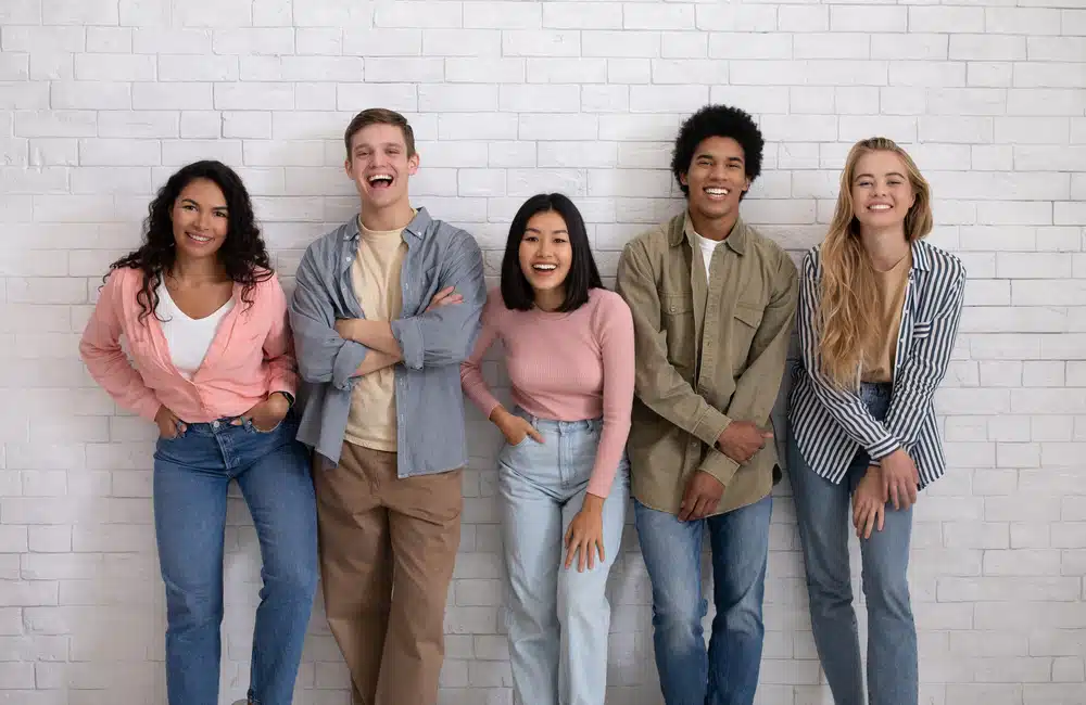 a group of students leaned on a wall smiling towards the camera