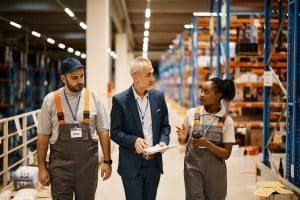 Mature businessman communicfating with young workers while walking through distribution warehouse.