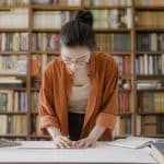 A high school student reviews notes and textbooks in a library while researching chemistry internships for high school students.