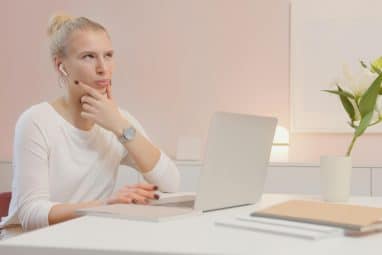 A young woman sits at a desk, thinking about the difference between Wellesley vs Barnard.