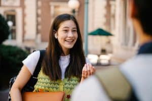 A young person wearing a green vest smiles outdoors reflecting on the brown motto