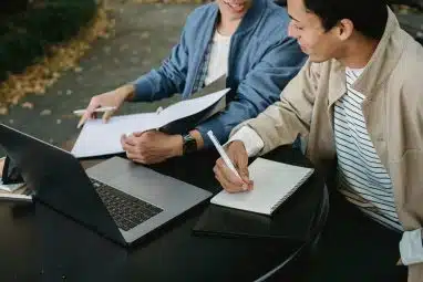 Two friends discussing while making notes in front of a laptop