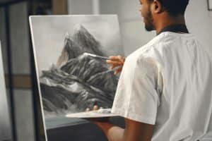 An art student painting a landscape with his back turned 