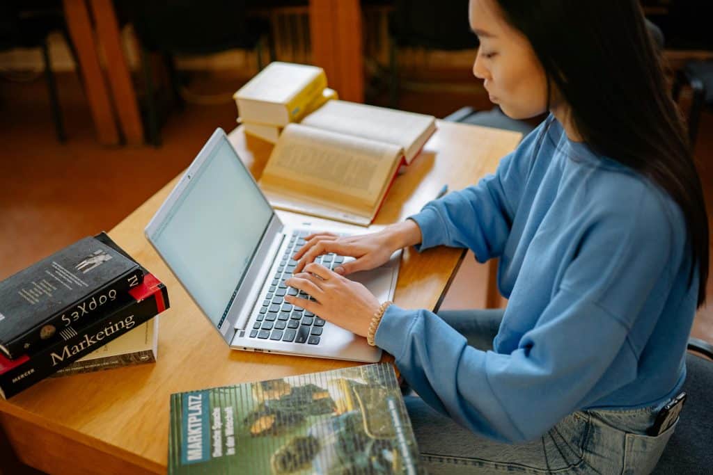 Student researching and drafting a letter of continued interest on a laptop while studying in a library