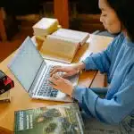 Student researching and drafting a letter of continued interest on a laptop while studying in a library