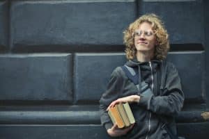 student in blue holding books as preparation to meet Harvard's GPA requirements
