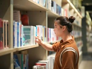 A young man in the library looking for psychology research topics for his thesis.