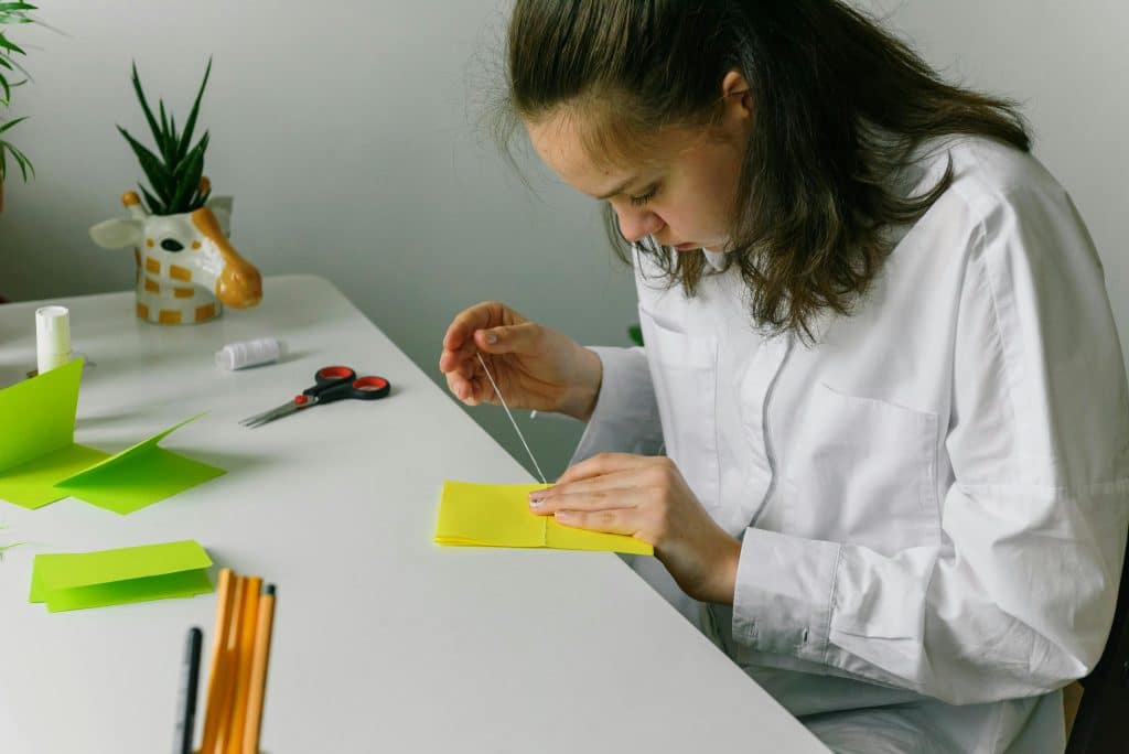 A student sews bright paper by hand at a desk, illustrating passion project ideas for high school students.