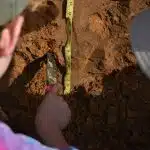 Archaeology students measuring and excavating soil at a dig site, representing fieldwork at the best colleges for archaeology