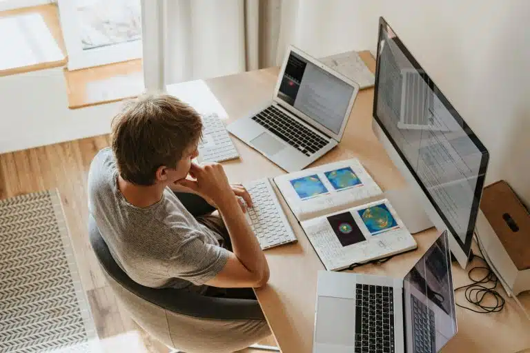 A man sitting on a desk surrounded by computers and learning materials