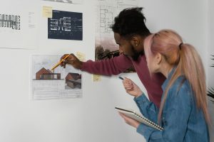 Two architecture students studying a blueprint taped to the wall