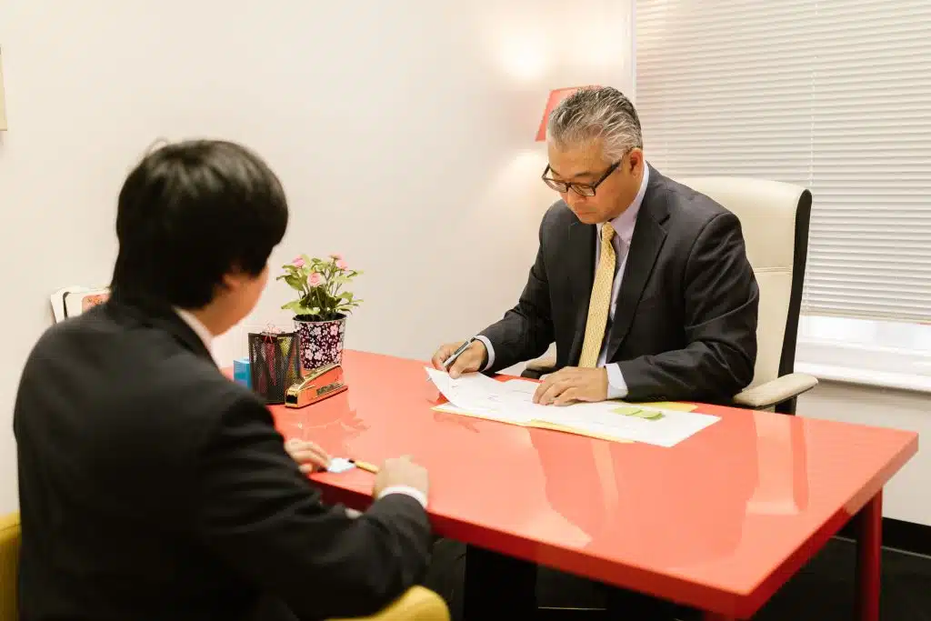 Harvard admissions consultant in a suit and gold tie reviewing documents with a student at a red desk