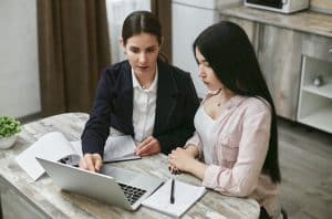 An Ivy League tutoring session where a tutor explains coursework on a laptop to a student, both focused and taking notes at a table.
