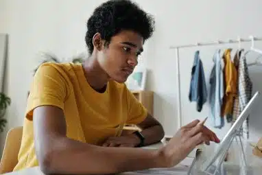 A young man uses a tablet while considering Cornell vs Johns Hopkins.