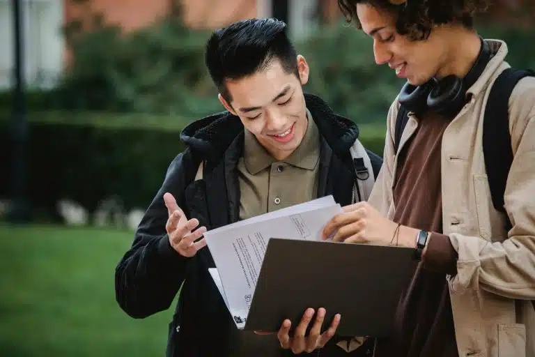 Two college students standing outside on campus reviewing papers in a folder, illustrating discussion about the UPenn grading scale.