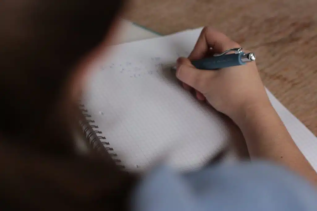 Student writing math equations in a notebook, studying for colleges that don’t accept AP credits.