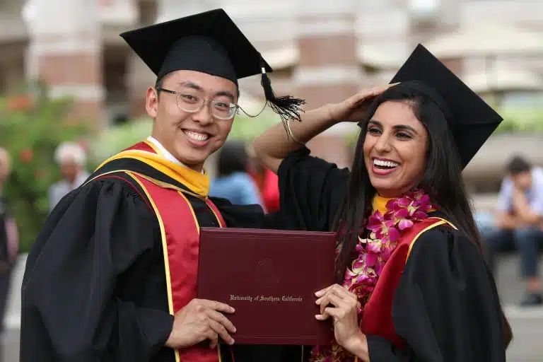 Two USC graduates in caps and gowns celebrate on campus, highlighting success under the USC grading scale.
