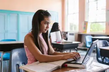 High school student using a laptop in class with an open notebook, studying and tracking her high school GPA.