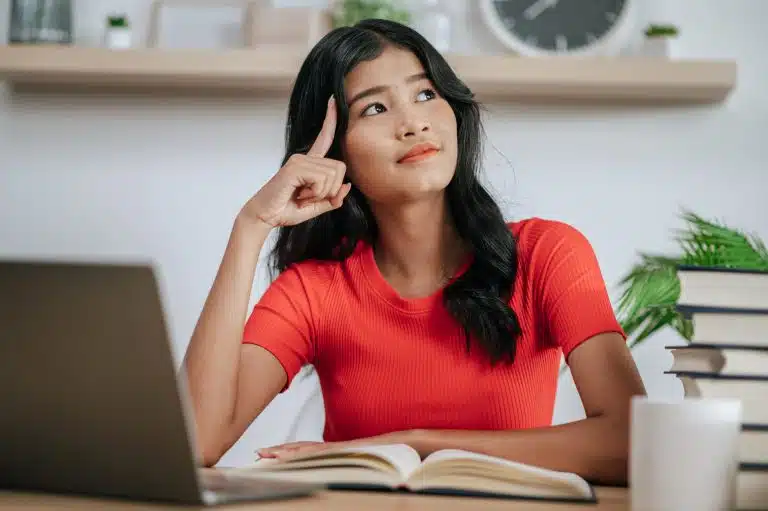 A young woman sits at a desk, thinking about the difference between Harvard vs the United States Military Academy.