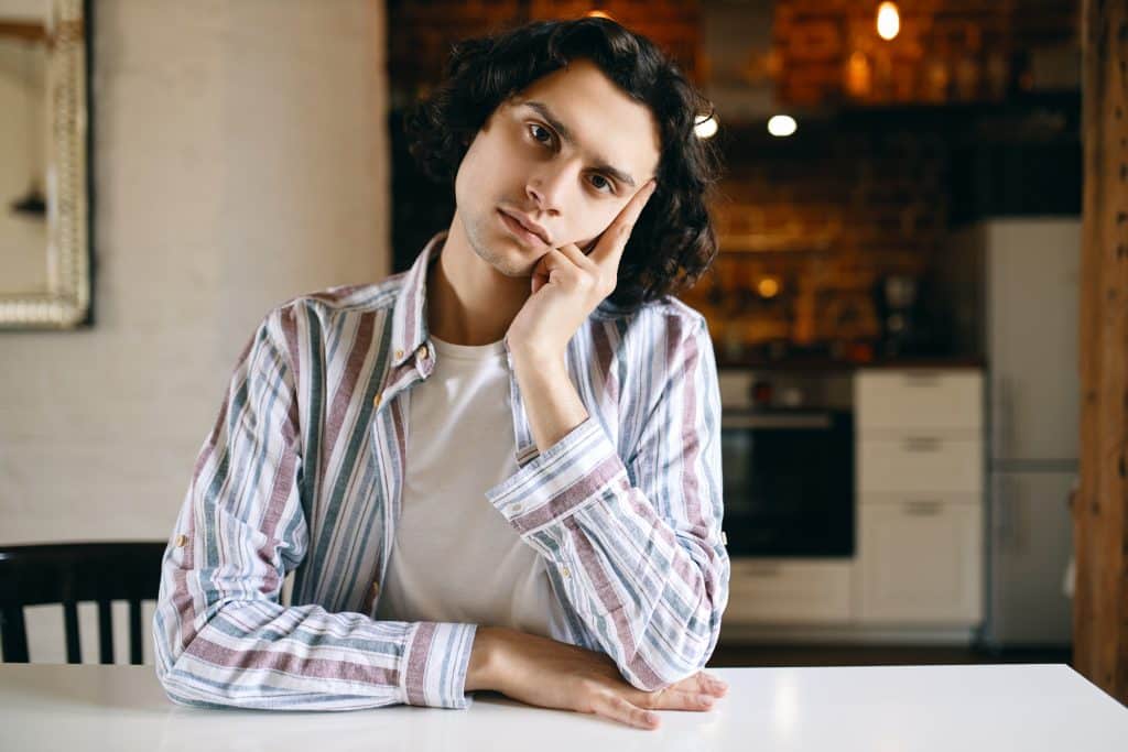 A young man sits at a table in thought, reflecting on his decision between NYU vs Northeastern.