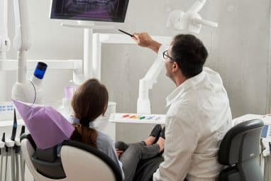 Dentist showing a patient dental X-rays on a screen, illustrating commitment and preparation like writing a letter of intent for dental school.