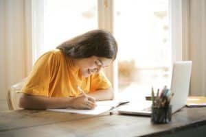Student in yellow shirt writing on white paper about what to include in common app honors section