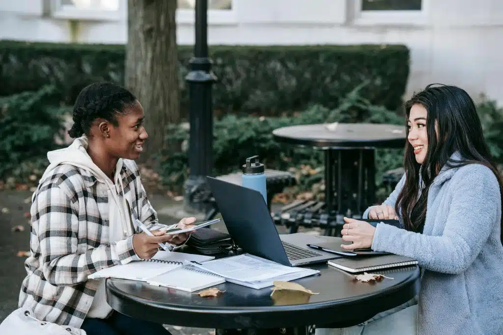 Two college students studying outdoors with notebooks and laptops, discussing applications related to Caltech early action.