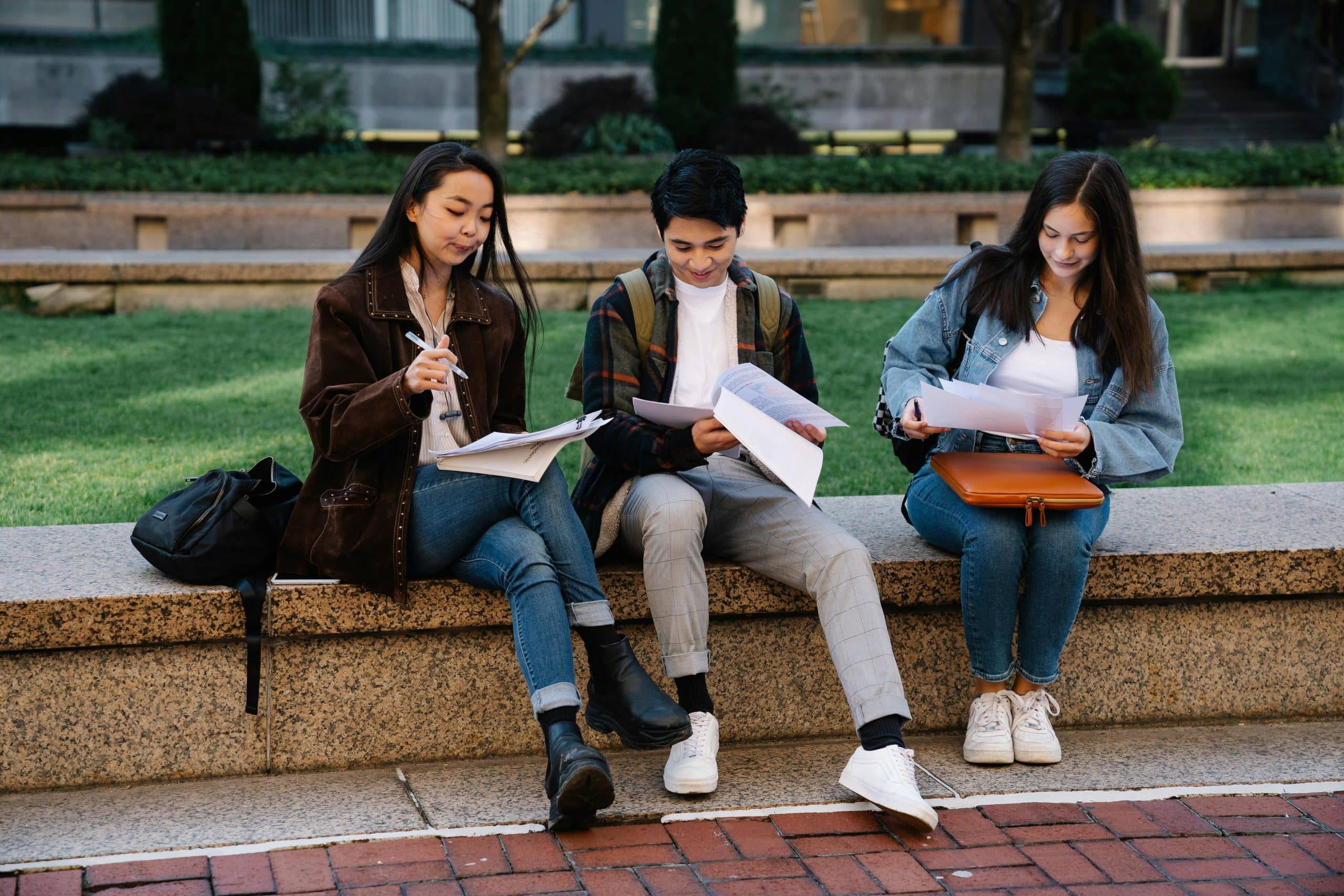 Three students sitting outside on campus reviewing papers together, symbolizing preparation for the Tufts application deadline.