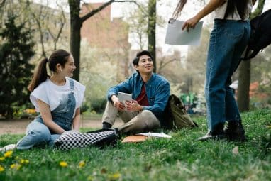 Three college students sitting on the grass and studying together on campus, discussing admissions and asking does Dartmouth have early action.