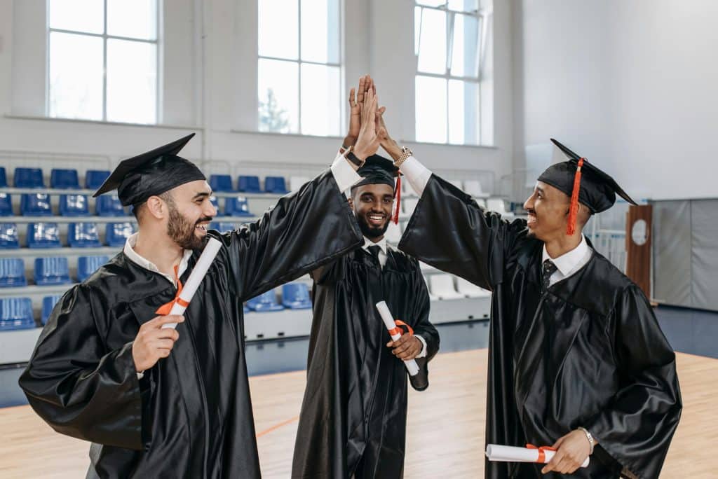 Three graduates in caps and gowns celebrate with a high-five, representing the success of Duke University notable alumni.